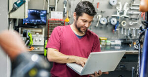 ein Mann, der in einer Fahrradwerkstatt steht und einen Laptop bedient
